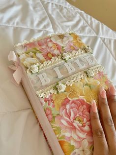 a woman's hand holding an open book with flowers and lace on the cover