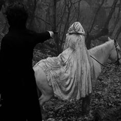 a woman in white dress riding on the back of a white horse through a forest