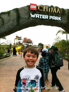 a young boy standing in front of the entrance to a water park with people walking by