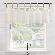 a kitchen window with white curtains hanging from the side and a black faucet in front of it