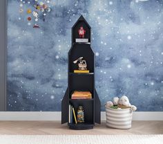 a room with a space themed wallpaper and bookshelf in the corner, next to a toy rocket ship