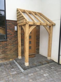 a wooden gazebo in front of a brick building with a door on the side