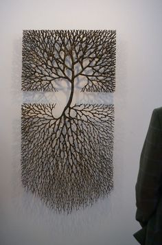 a man standing in front of a wall with a metal tree sculpture on it's side