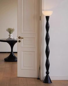 a floor lamp next to a door with a vase on the table in front of it