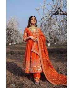 a woman wearing an orange outfit and standing in the middle of a field with trees