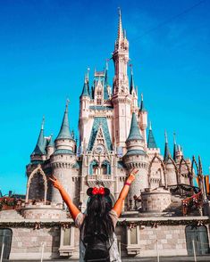 a woman standing in front of a castle with her arms up and hands out to the side