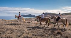 three people are riding horses on the top of a hill overlooking the ocean and mountains