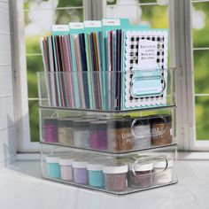 a clear plastic container with various craft supplies in front of a window and some windowsills