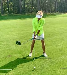 a man in a green shirt and white face mask hitting a golf ball with a club