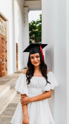 a woman in a graduation cap and gown leaning against a wall with her arms crossed