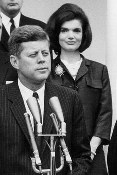 black and white photograph of three people in front of microphones with two men standing behind them