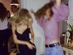 two women are dancing in a room with other people