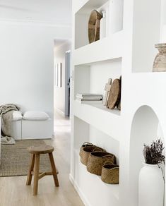 a living room with white walls and wooden flooring next to a shelf filled with baskets