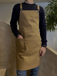 a man wearing an apron standing next to a plant