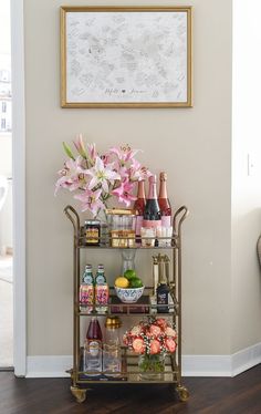 a bar cart filled with bottles and flowers on top of a hard wood floor next to a wall