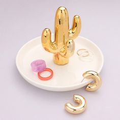 a white plate topped with gold colored jewelry and a cactus shaped object next to it