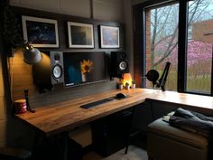 a computer desk with speakers and pictures on the wall behind it in front of a window