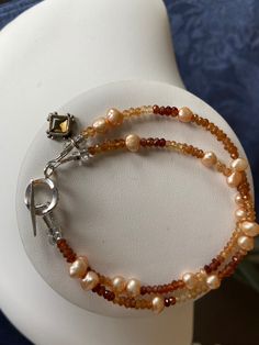 This two-strand bracelet combines faceted rounds of hessonite garnet (with its warm autumn hues of browns and amber) with beige freshwater pearls.  A charm made from faceted citrine set in sterling silver adds a little something extra. Item number 1220-BR48 Elegant Orange Beaded Bracelets With Gemstones, Elegant Orange Gemstone Beaded Bracelets, Elegant Orange Bracelets With Faceted Beads, Elegant Brown Gemstone Beaded Bracelets, Elegant Orange Beaded Bracelet With Natural Stones, Elegant Orange Gemstone Beaded Bracelet, Hessonite Garnet, Strand Bracelet, Warm Autumn