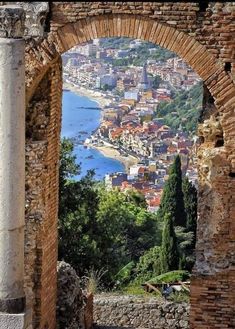 an arch in the wall leading to a view of a town and water from above