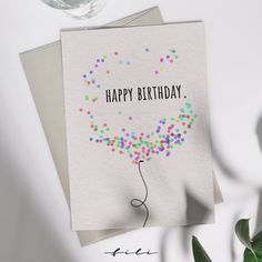 a happy birthday card with confetti on it and a wine glass next to it