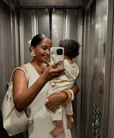 a woman holding a baby taking a selfie in a bathroom mirror with her cell phone