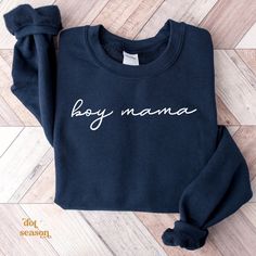 a black sweatshirt with the word boy mama written in white on it, sitting on a wooden floor