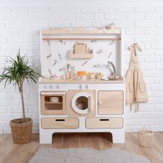 a wooden toy kitchen with an oven, sink and potted plant next to it