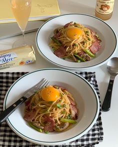 two white plates topped with pasta and an egg on top of it next to a bottle of wine