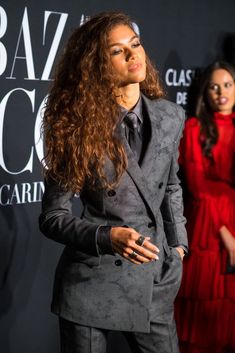 a woman with long hair in a suit and tie standing on a red carpet, looking off to the side