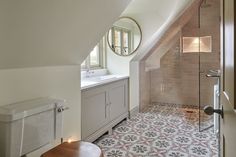 a bathroom with a sink, toilet and shower in the corner under an slanted roof