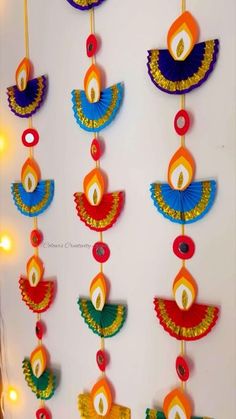 an assortment of colorful paper decorations hanging from strings on a white wall with lights in the background