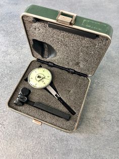 an open suitcase with tools in it sitting on the floor next to a clock and other items