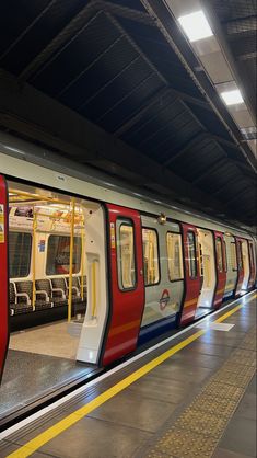 a red, white and blue train is pulled up to the platform at a station