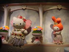 two hello kitty dolls are on display with flowers in vases and an elephant statue