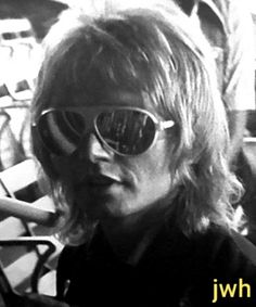 an old photo of a man with sunglasses on his face and long blonde hair in front of a group of people