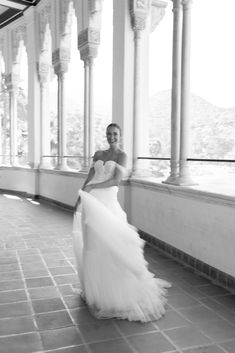 a woman in a wedding dress is posing for a photo by some pillars and windows