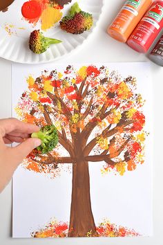 someone is painting a tree on paper plate with leaves and broccoli in the foreground