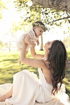 a woman holding a baby in her arms while sitting on the ground under a tree