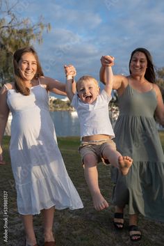 two women and a child are holding hands in the air while standing on grass near water