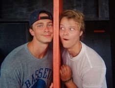 two people standing next to each other behind a wooden pole