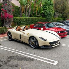 a white sports car parked in a parking lot next to some other red and black cars