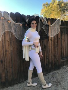 a woman in white outfit standing next to a fence with her hands on her hips