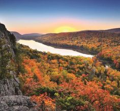 the sun is setting over an autumn landscape with trees and mountains in the foreground