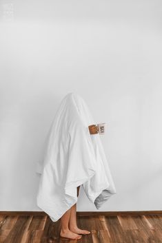 a person standing under a white towel on top of a hard wood floor next to a wall