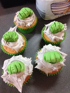 six cupcakes with green frosting on them sitting on a table next to a bag