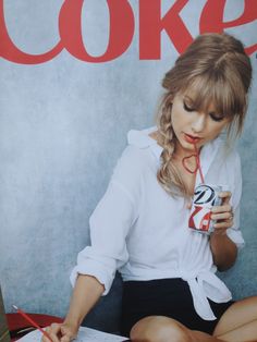 a woman sitting on the floor holding a book and drinking from a cup with a straw in her mouth