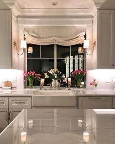 a kitchen sink sitting under a window next to a counter top with flowers on it