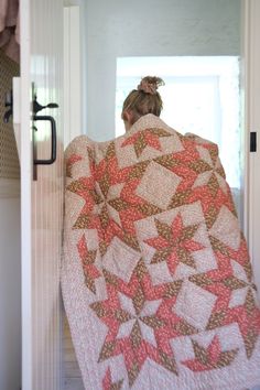 a woman is standing in front of a door with a quilt on it