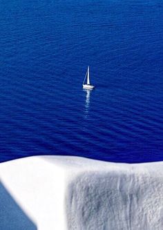 a sailboat floating in the middle of an ocean with snow on the ground and blue water behind it