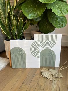 two canvass sitting on top of a wooden floor next to a potted plant